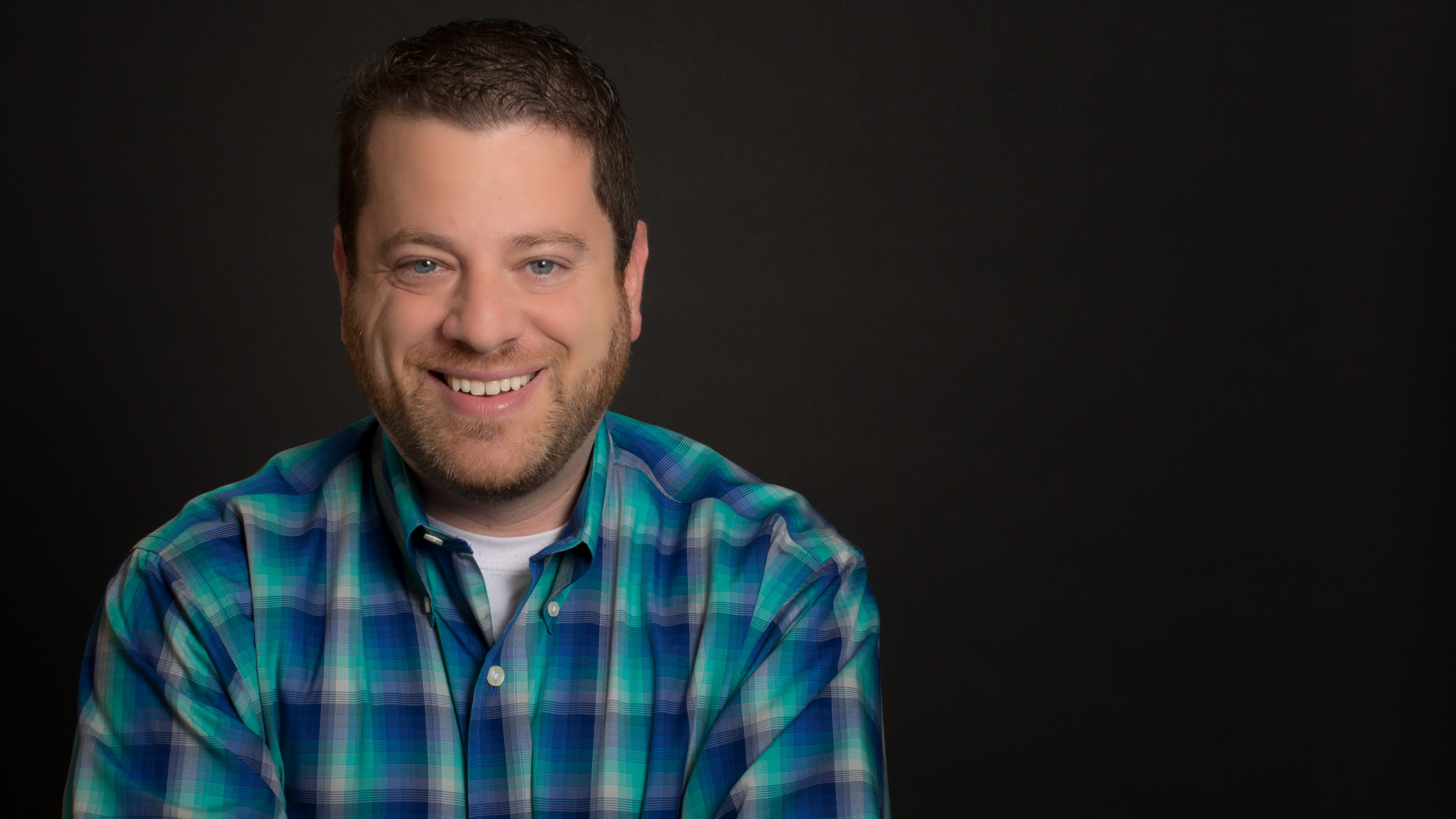 Professional headshot of Harlan Landes in a blue and green shirt against a dark background